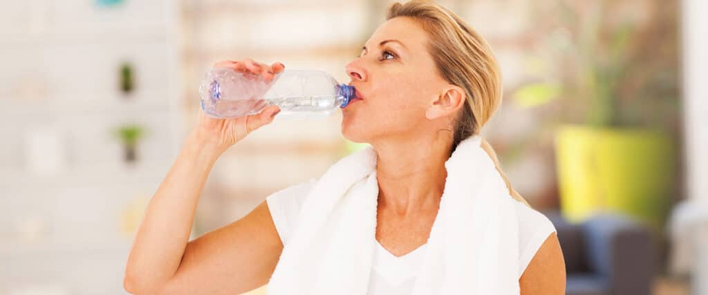 A woman drinking water after exercising, part of a woman's process of building healthy habits.